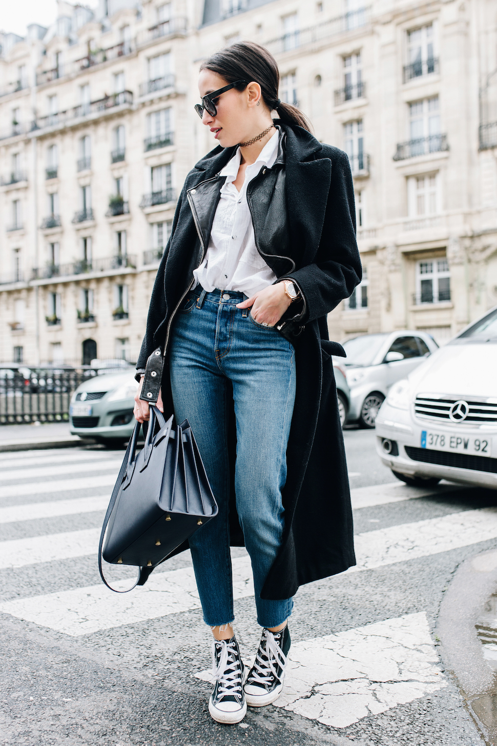 Alexandra Guerain wears a pair of sixties classic ankle high converse with cropped mom jeans and a simple white blouse, combined with layered black jackets to get that authentic style. Blouse/Jacket: Asos, Jeans: Levi’s, Shoes: Converse. 