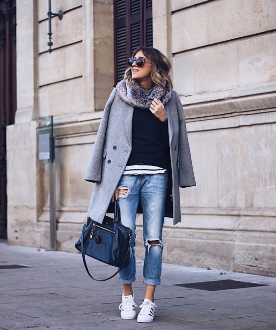 Ane Hernando is seen in a pair of faded denim jeans, with rip detailing, and rolled at the ankle. This she has then paired with gleaming Adidas sneakers, a navy blue top, and an oversized boyish grey coat. Shoes: Adidas.