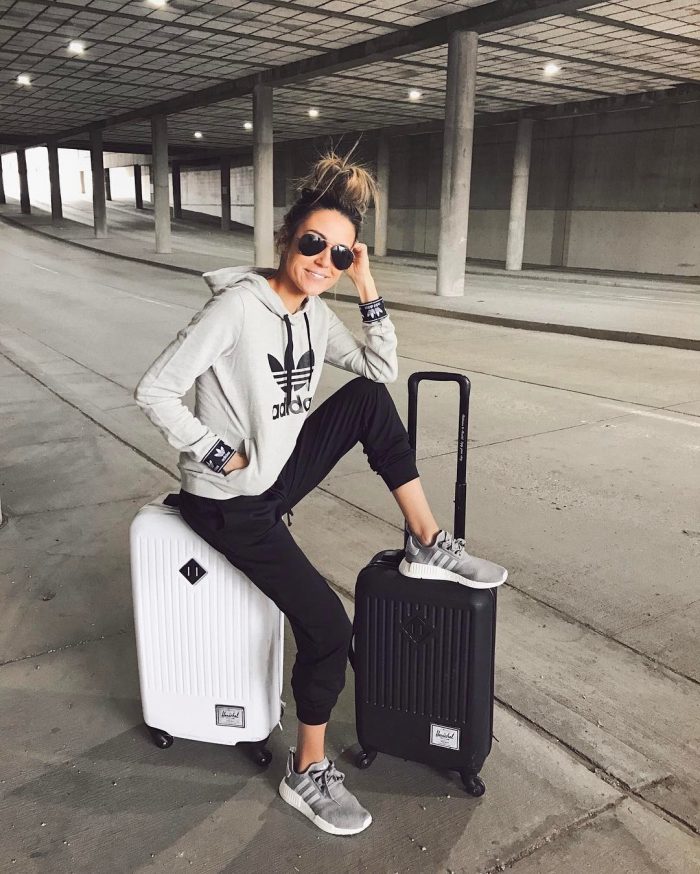 Christine Andrew is seen in a simple but stylish grey Adidas hoodie, with black joggers and matching grey sneakers, This sporty chic style is perfect for travelling long journeys. Sweater: Adidas.